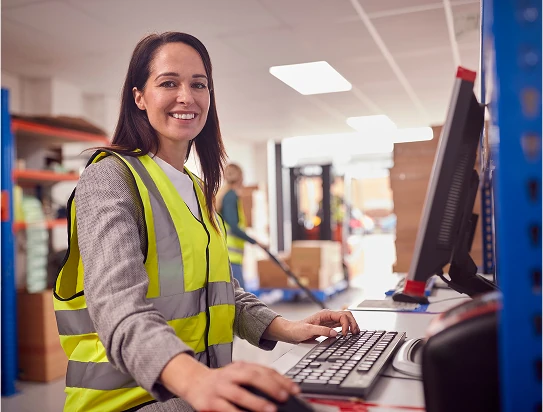 A person wearing a safety vest stands at a computer
